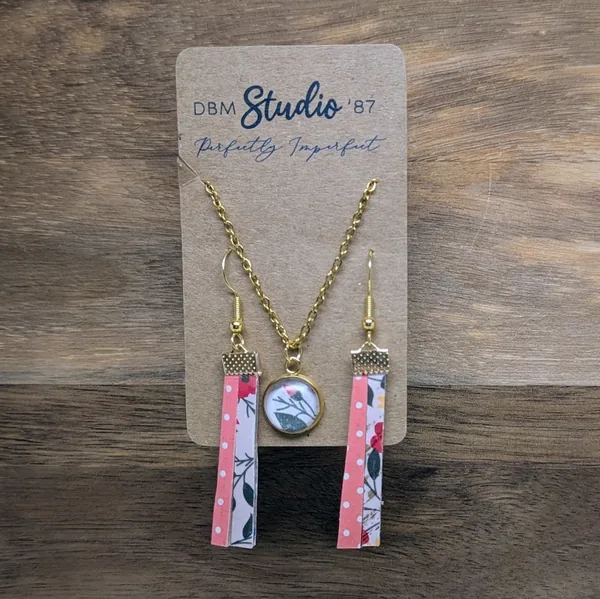 medium split paper felt earrings. Half pink, red, green florals in blush background, other half pinka nd white polka dots. Gold finishes. 18k gold plated chain necklace with matching floral cabochon pendant.